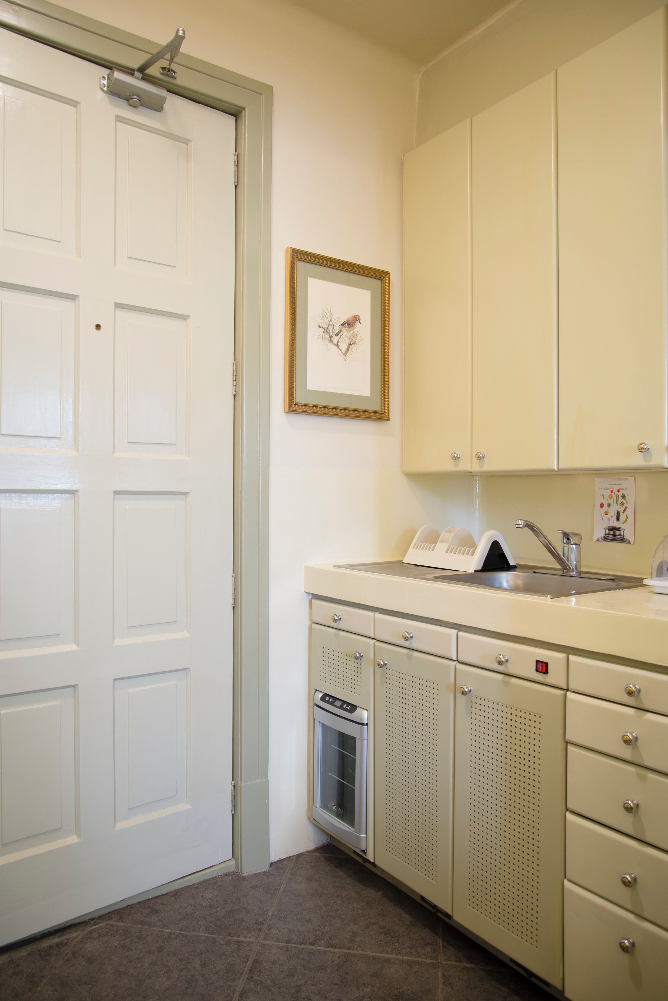 A kitchen with white cabinets, a sink, a microwave, and a framed picture on the wall.