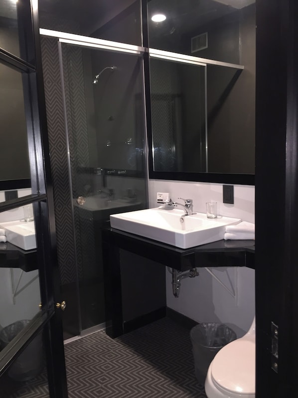 Un baño moderno con una paleta de colores blanco y negro, que cuenta con un espejo grande, un lavamanos blanco y un inodoro.
