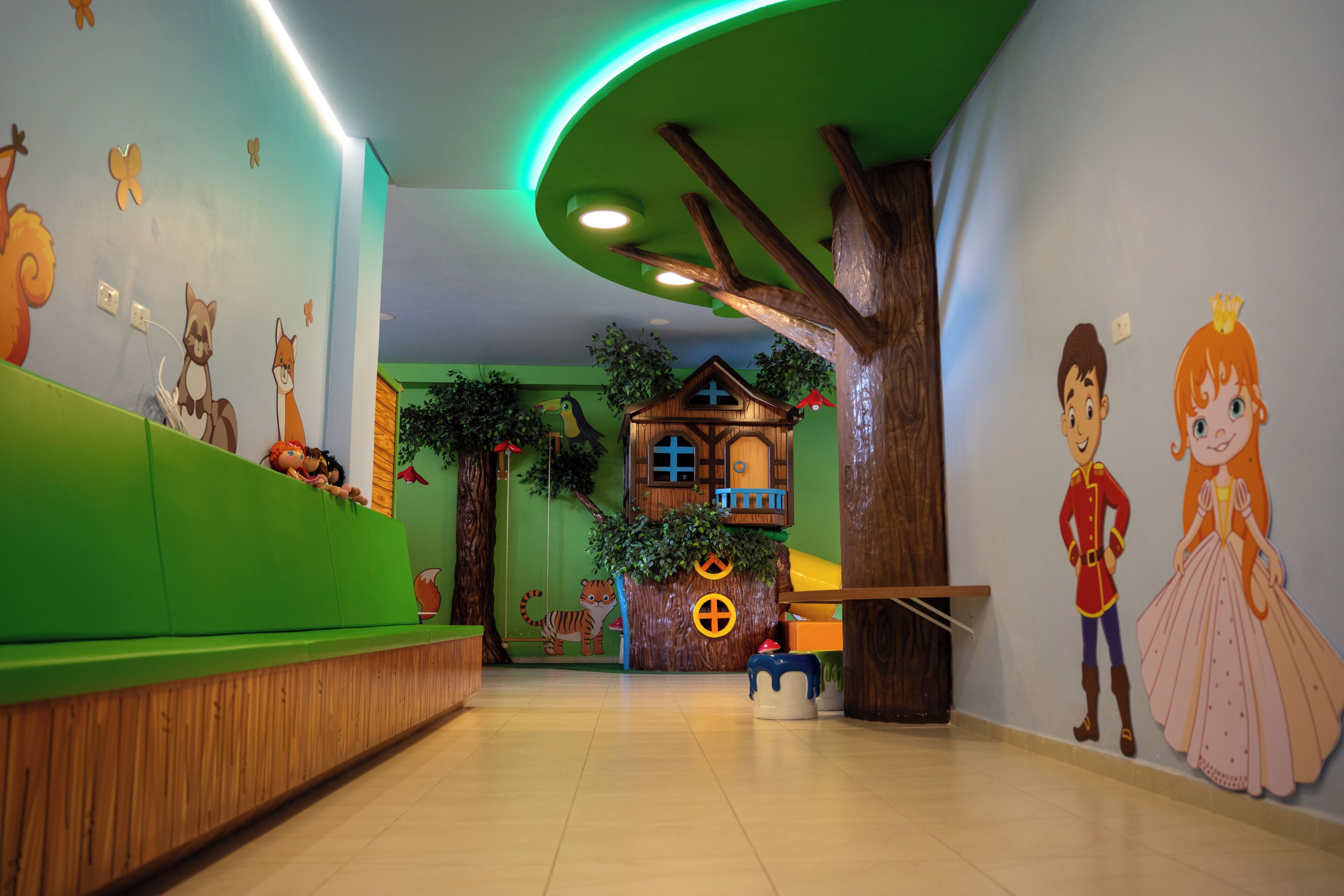 Espaço de recreação infantil com parede verde, banco de madeira e um mural de árvore.