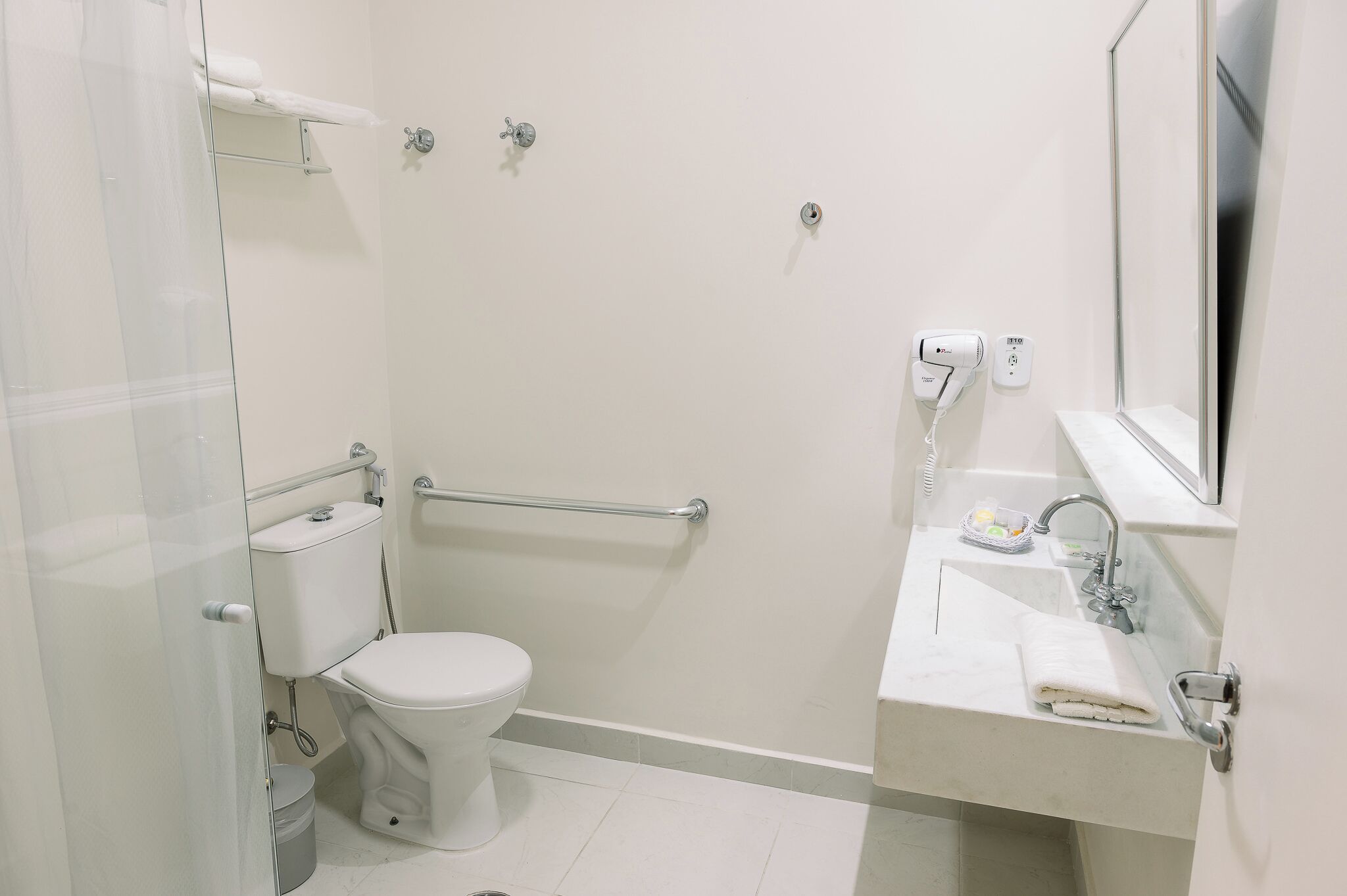 A modern bathroom with a toilet, a glass shower enclosure, a sink with a mirror, and a towel rack.