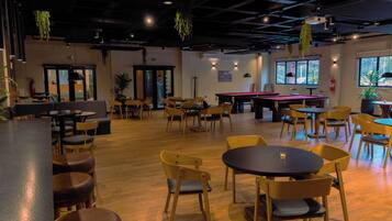 Un espacio interior amplio con diversas opciones de asientos, incluyendo mesas redondas y sillas, una mesa de billar y una zona de bar.