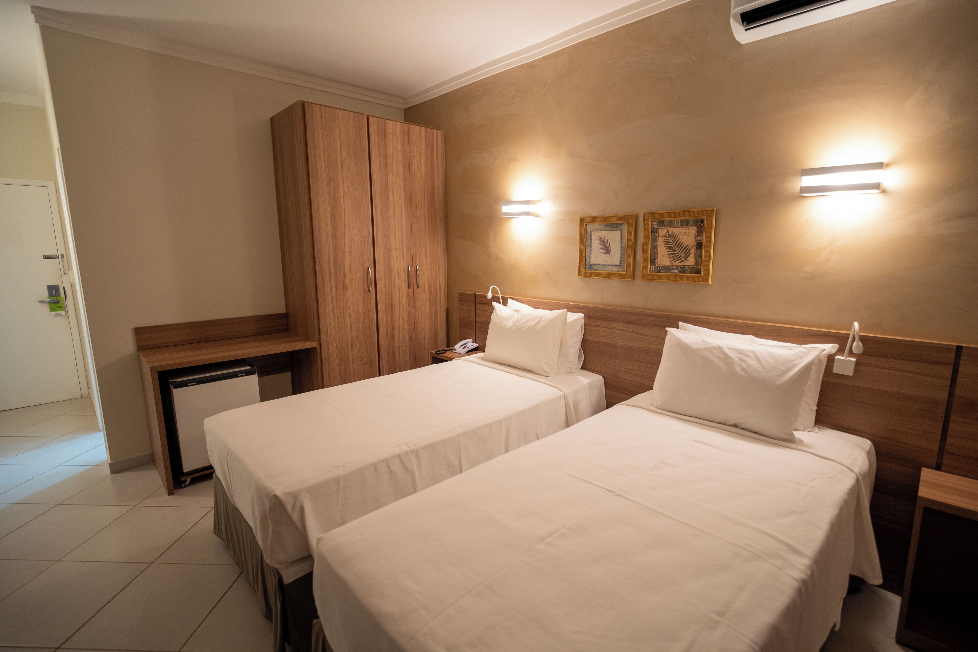 Habitación de hotel con dos camas, un armario de madera, un escritorio y un refrigerador pequeño.