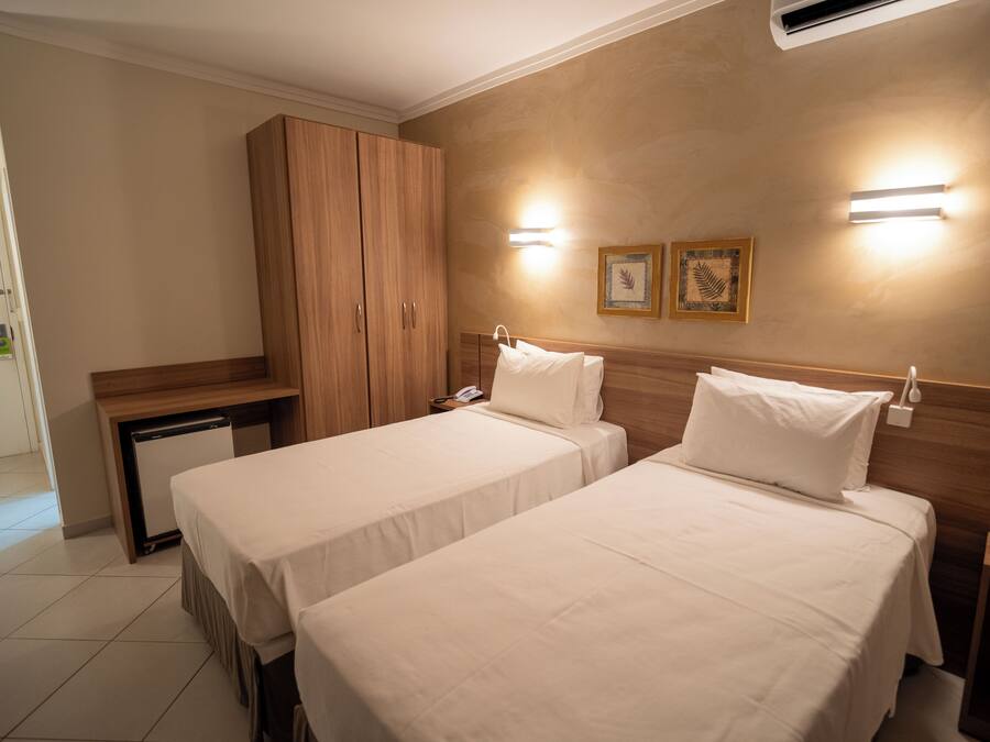 Een hotelkamer met twee bedden, een houten kast, een bureau en een kleine koelkast.