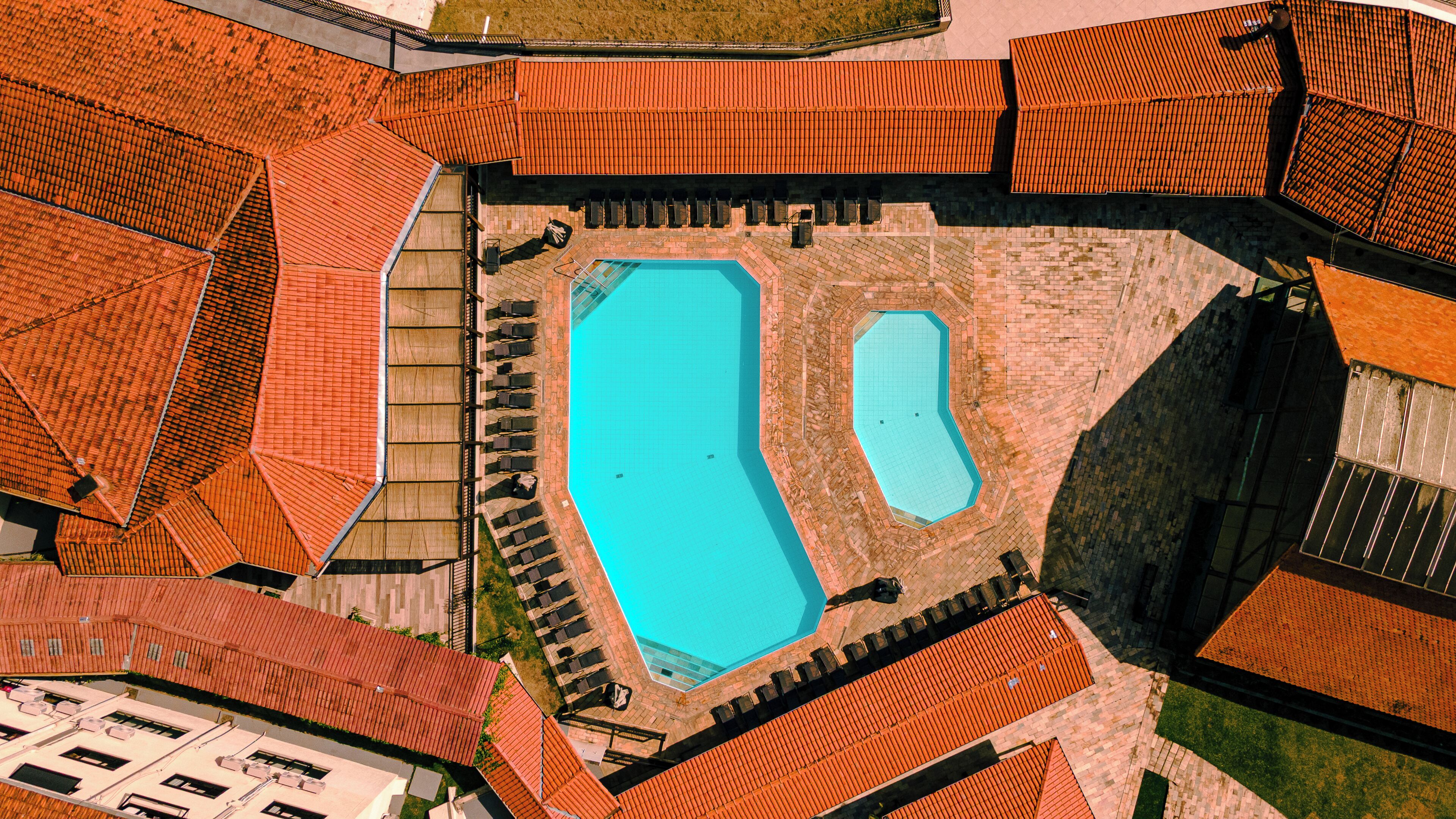 An aerial view of a property with two swimming pools, red-tiled roofs, and a brick patio area.