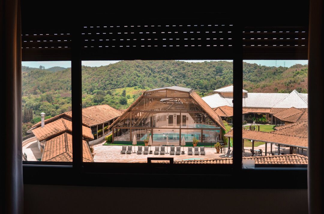 A view of a building with a glass facade, a pool, and a mountainous landscape in the background.