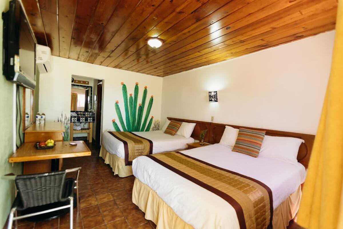 A hotel room with two beds, a wooden ceiling, a dining table with chairs, and a small kitchen area.