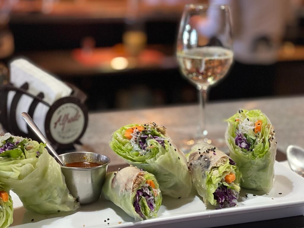 A plate of fresh spring rolls with a dipping sauce, accompanied by a glass of white wine.