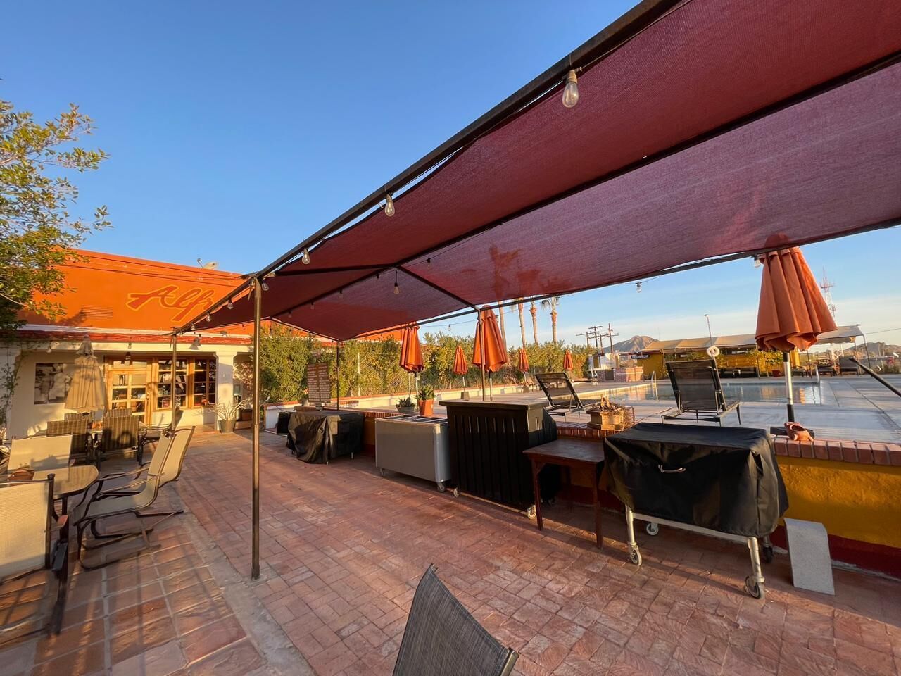 An outdoor patio area with a covered seating area, a grill, and umbrellas.