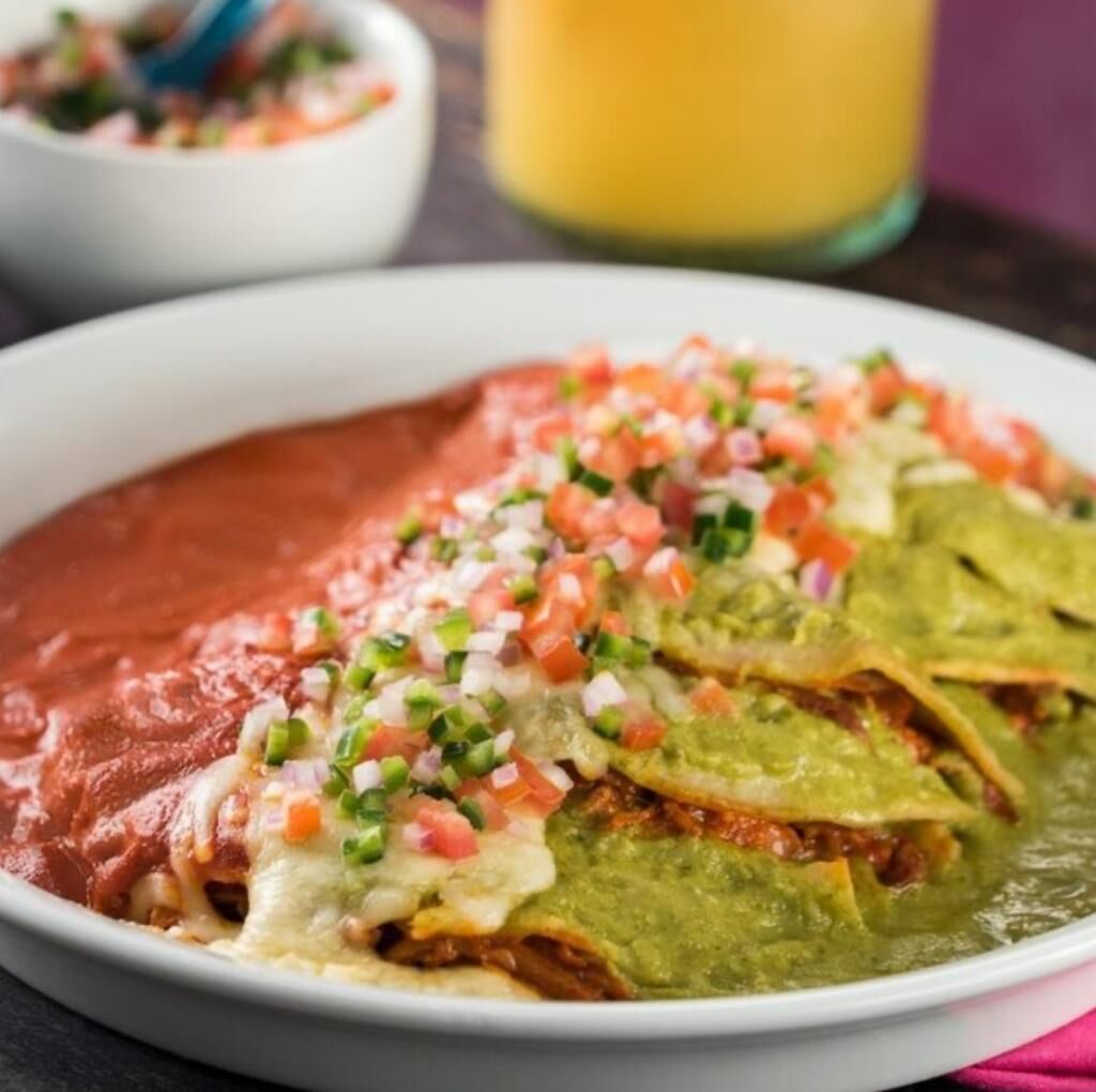 Un plato de nachos con queso, guacamole y tomates picados.