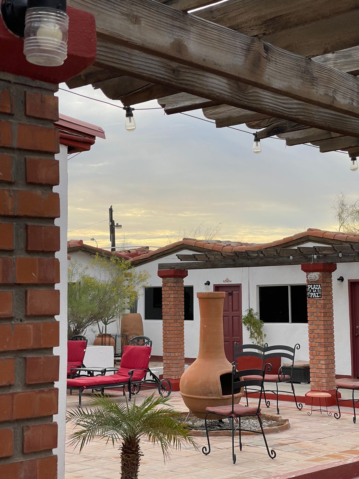 A patio area with outdoor seating, a large terracotta pot, and a building with a red door and windows.