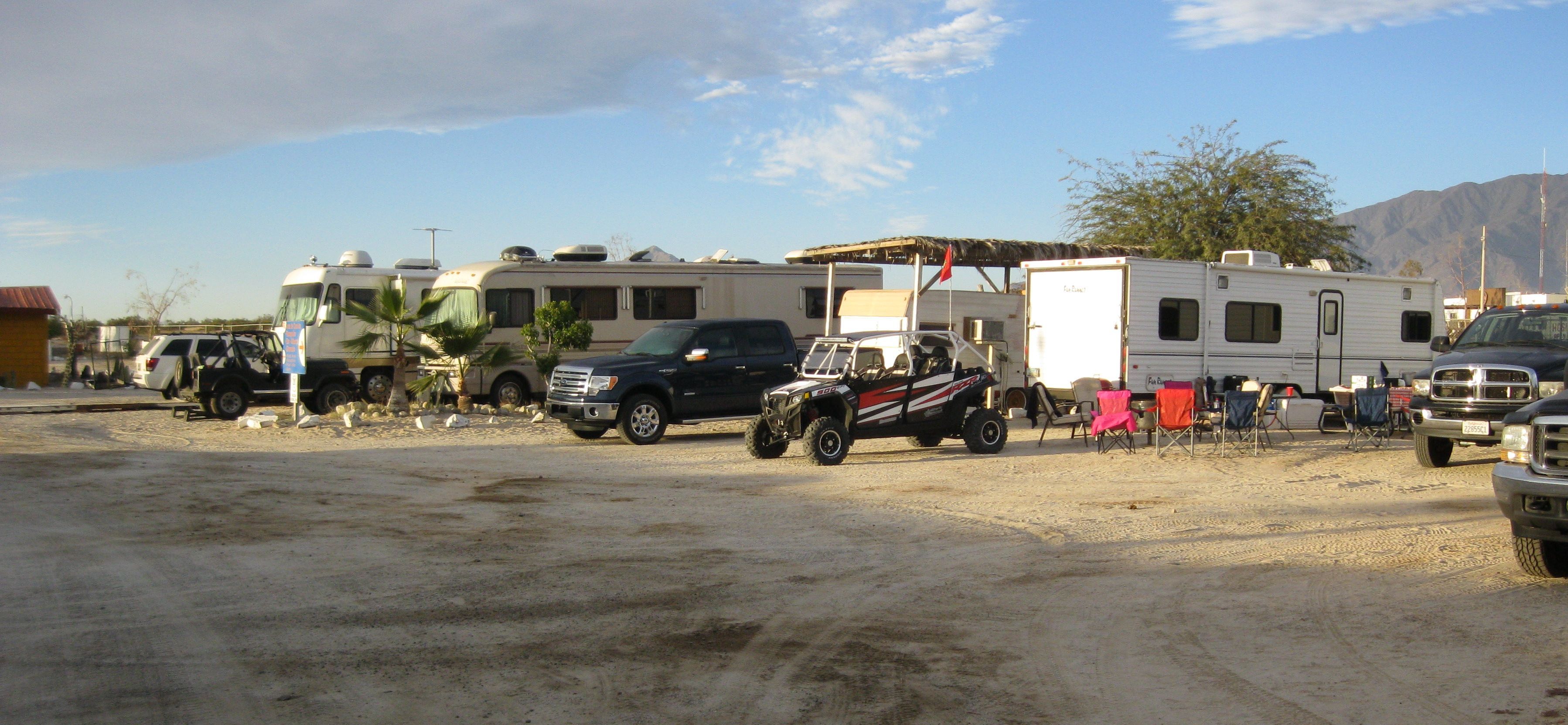 Un terrain de camping où sont stationnés divers camping-cars et VUS sur un sol sablonneux.