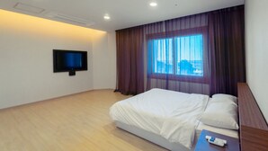 Une chambre d’hôtel avec un lit, un téléviseur fixé au mur, une fenêtre avec des rideaux et un plancher en bois.