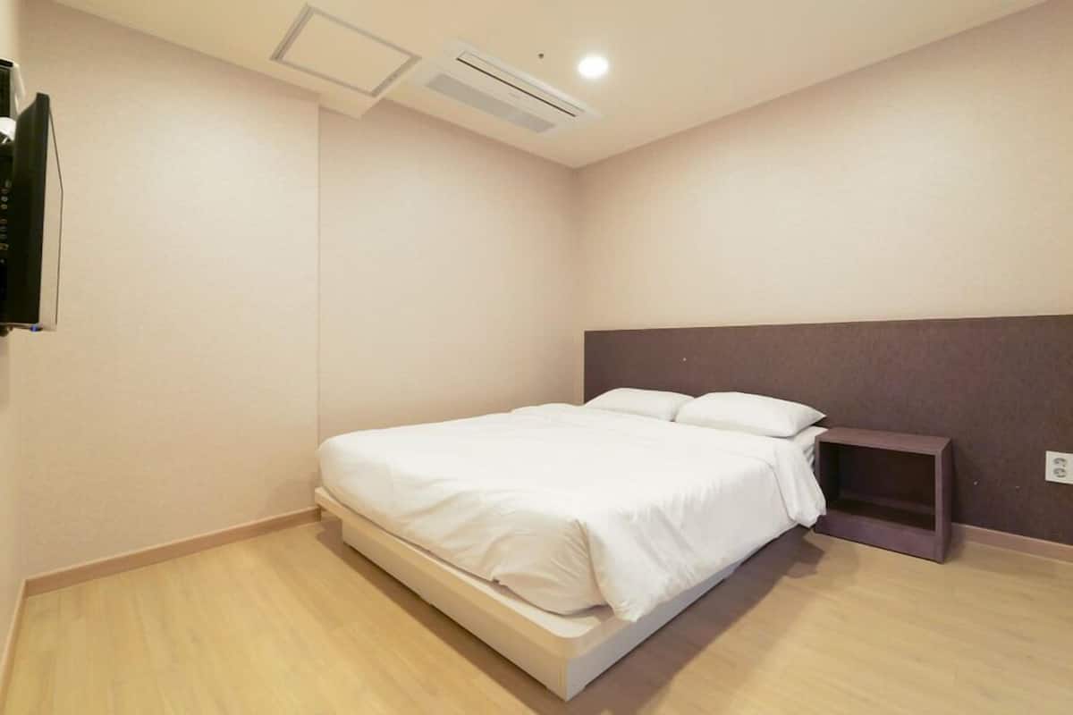 Un dormitorio con cama, mesita de noche y televisor montado en la pared.