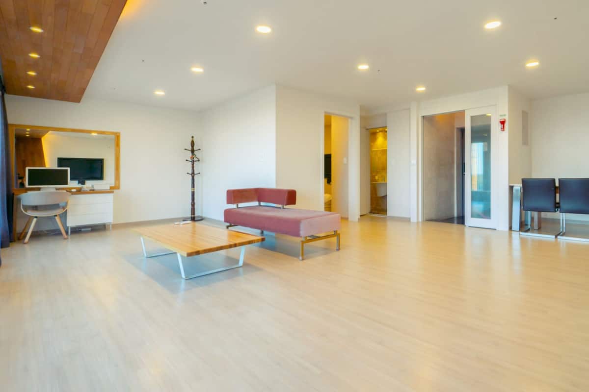 Una habitación amplia con suelo de madera, un escritorio con ordenador, un sofá rojo y dos sillas.