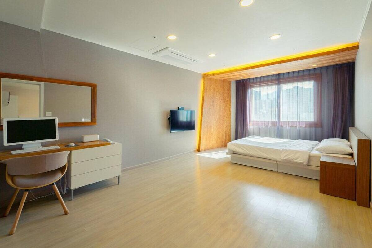 Un dormitorio moderno con escritorio, televisión de pantalla plana, cama y un gran ventanal con cortinas.