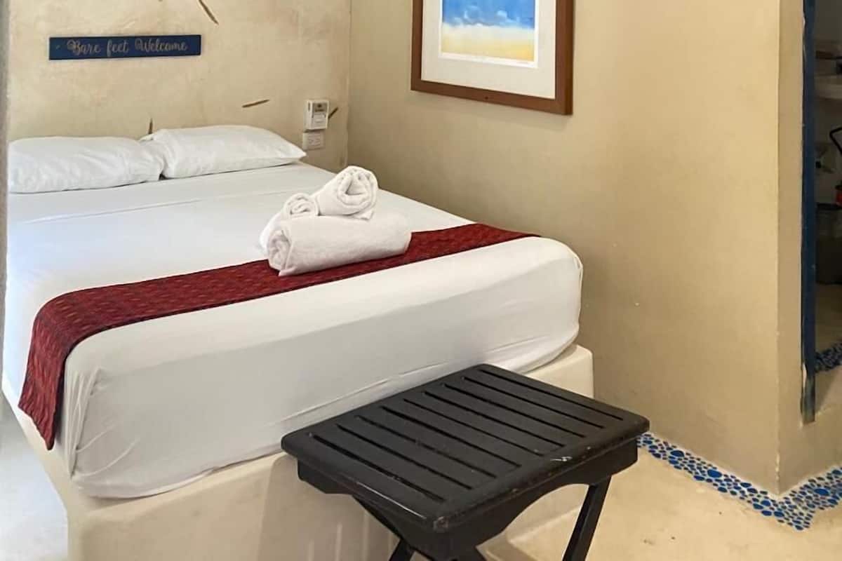 A hotel room with a bed, a ceiling fan, a framed picture, and a small table.