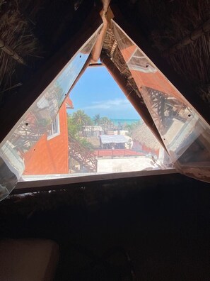 A room with a triangular window overlooking a beach and palm trees. - La Constanza de Rulo (Isla Holbox)