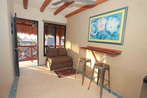 A room with a sofa, two barstools, a painting, and a view through a door. - La Constanza de Rulo (Isla Holbox)
