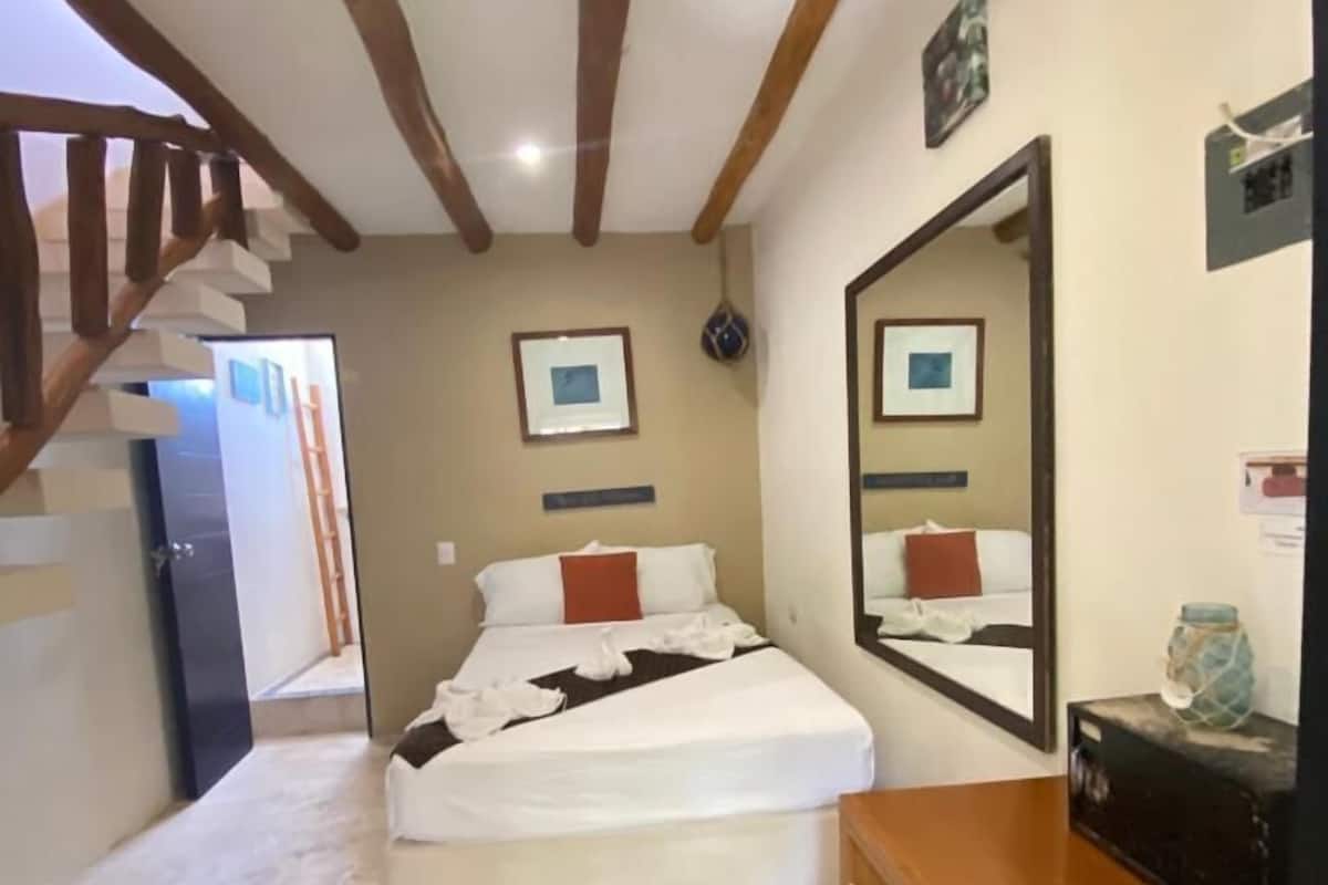 A bedroom with a bed, a dresser, a mirror, and a staircase.