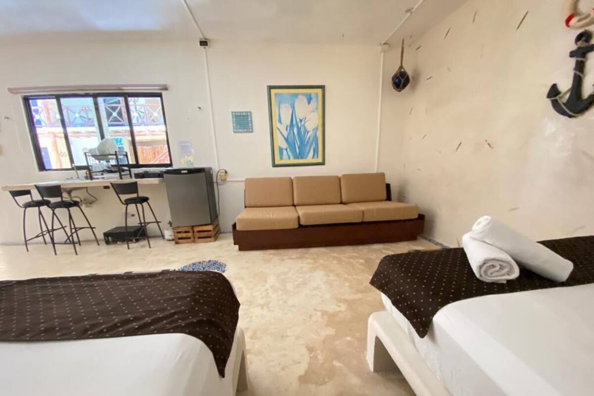 A hotel room with two beds, a sofa, a desk with chairs, and a large window.