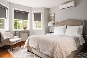 A bedroom with a large bed, a chair, a desk, and a window with a view of greenery. - Craigleith Manor Bed & Breakfast (Collingwood)