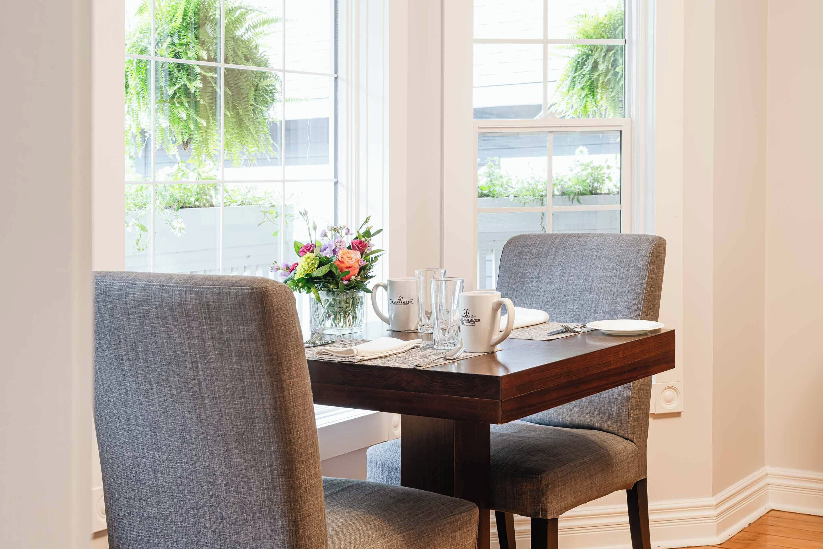 A dining table set with chairs, a vase of flowers, and a coffee mug.