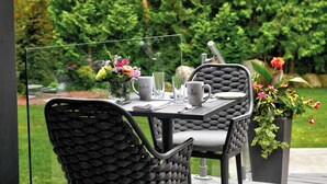 Un espace de restauration en plein air avec une table dressée pour deux personnes, entourée de verdure.