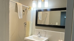 A bathroom with a white sink, a mirror, a toilet, and a shower area. - Budget Inn (Artesia)