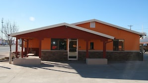 A building with a covered entrance, a sign with a logo, and a clear sky. - Budget Inn (Artesia)
