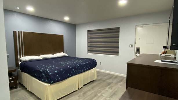 A bedroom with a bed, bedside table, and a desk with a chair. - Budget Inn (Artesia)