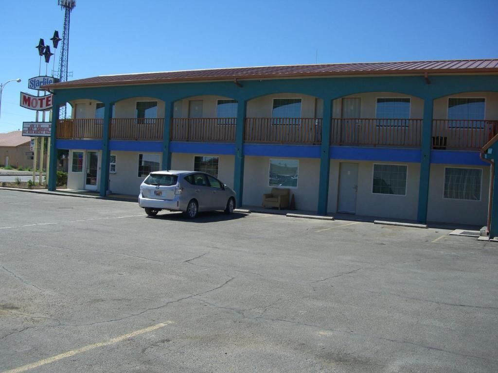 A motel with a two-story structure, a car parked in front, and a clear blue sky.