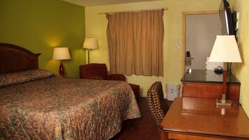 A hotel room with a bed, a desk, a chair, a lamp, and a curtain.
