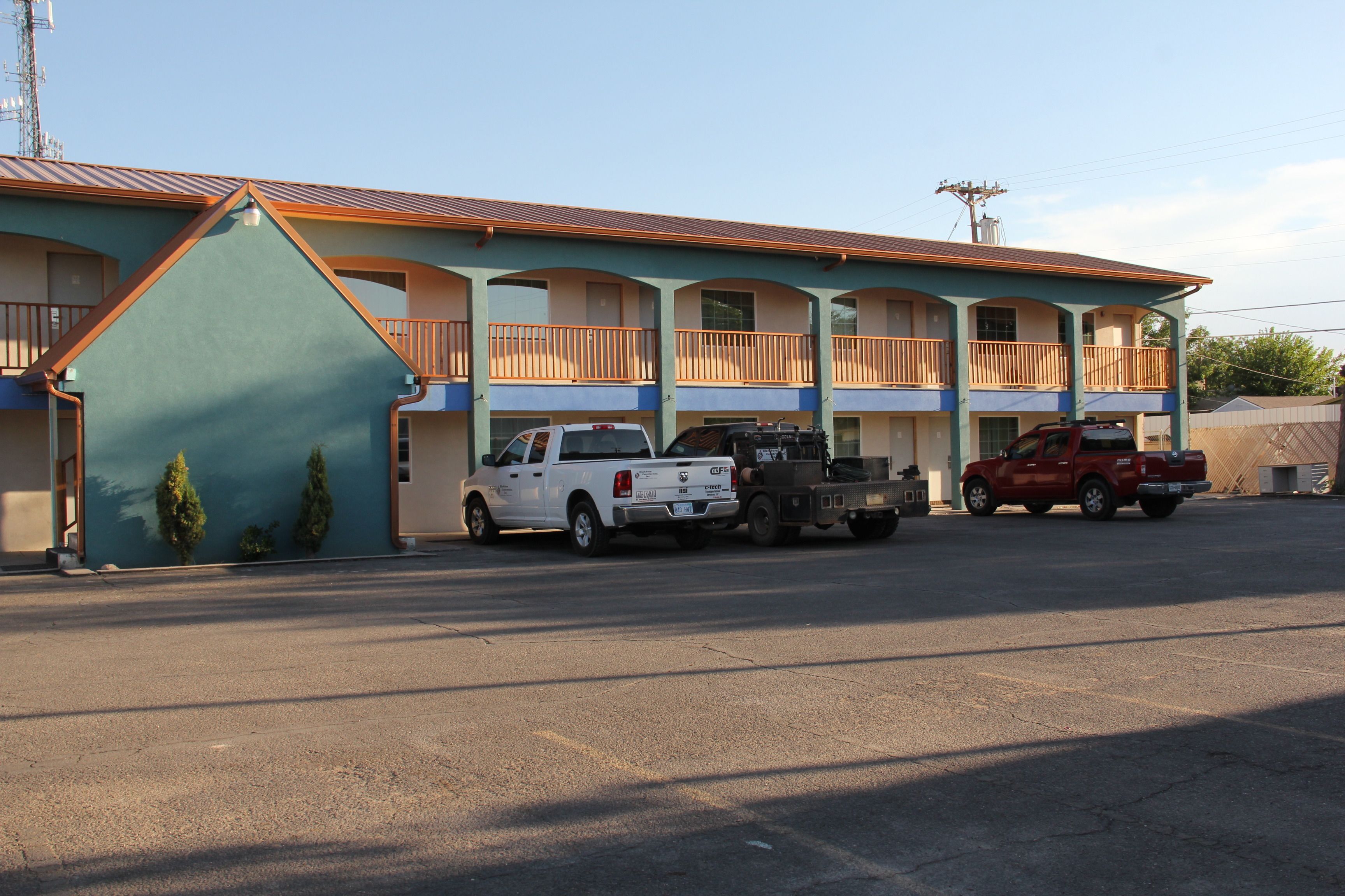 A motel with a blue exterior, multiple balconies, and a parking lot with several vehicles.