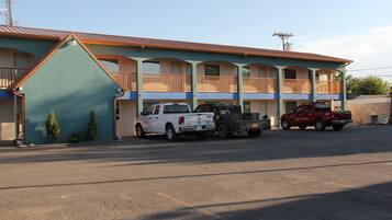A motel with a blue exterior, multiple balconies, and a parking lot with several vehicles.