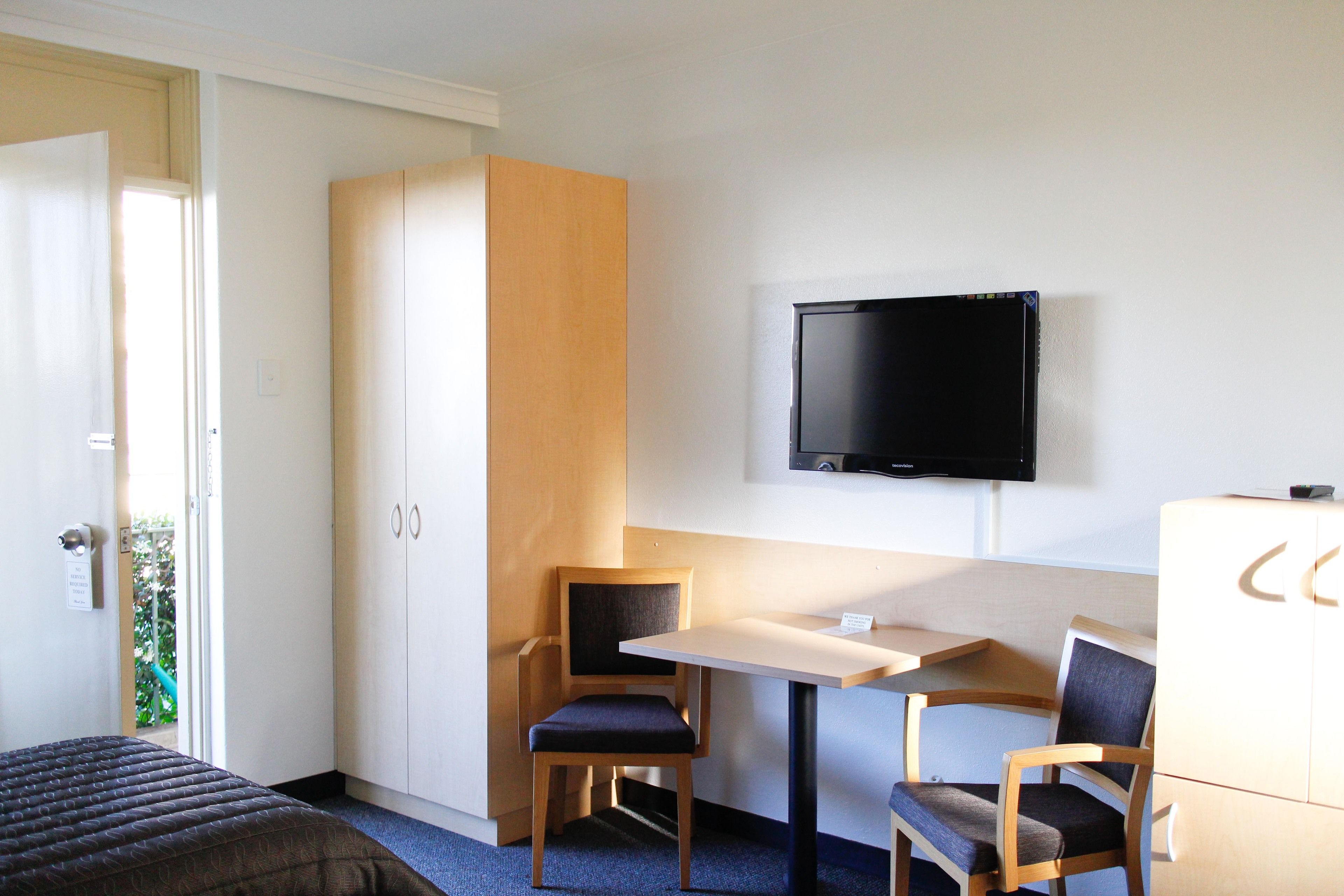 A hotel room with a bed, a desk, two chairs, a television, and a wardrobe.