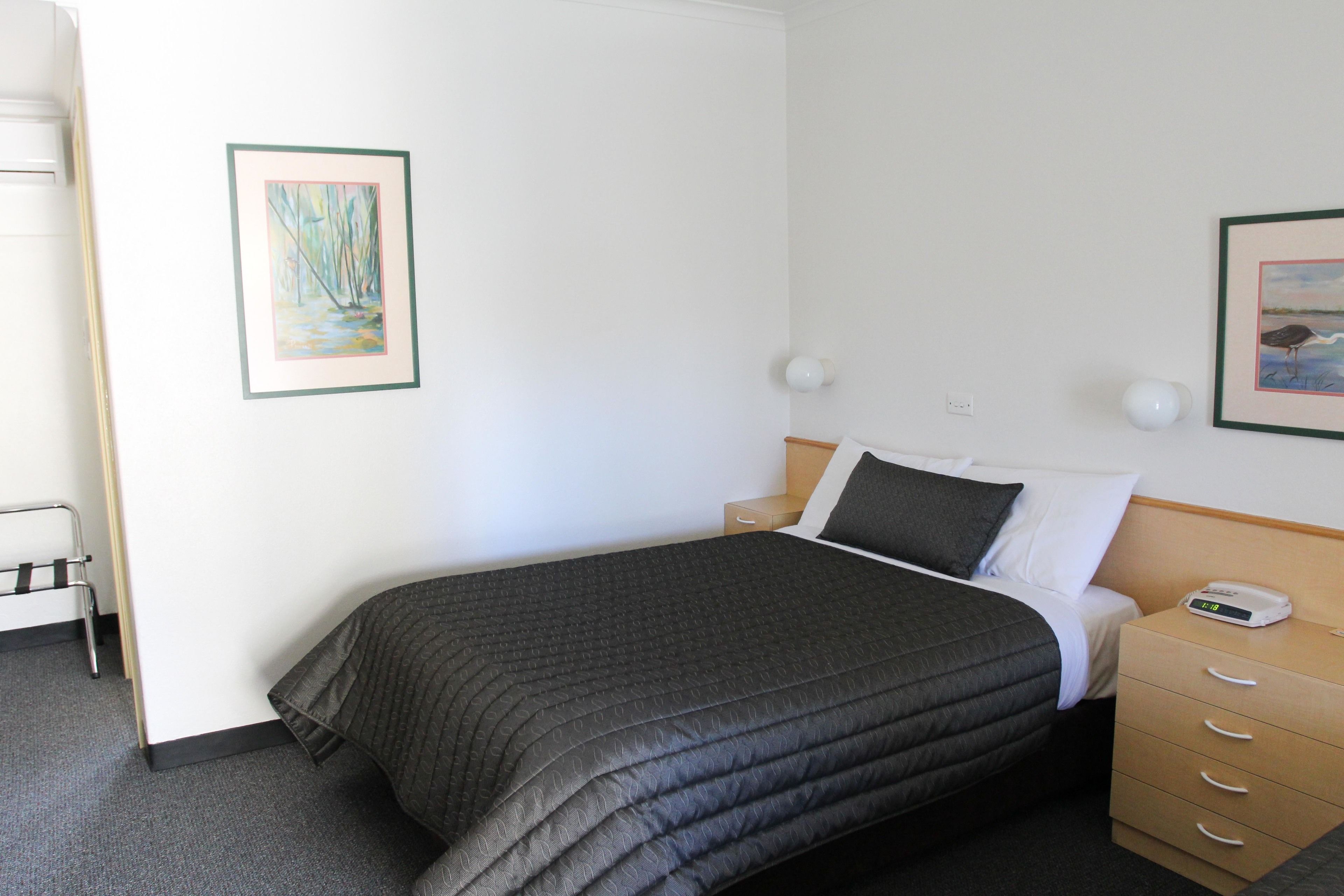 A neatly made bed with a dark quilt, a bedside table with a lamp, and two framed pictures on the wall.