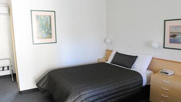 A neatly made bed with a dark quilt, a bedside table with a lamp, and two framed pictures on the wall.
