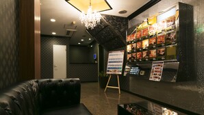 A lobby with a black leather sofa, a chandelier, a reception desk with a menu board, and a wall with framed pictures. - Hotel Atlantis Higashiosaka - Adults Only (Higashi-osaka)