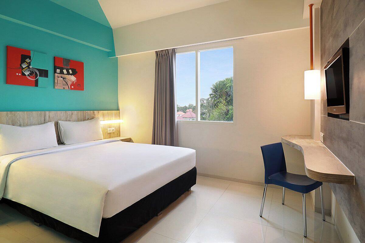 Une chambre d’hôtel avec un lit, un bureau, une chaise, une télévision et des œuvres d’art accrochées au mur.