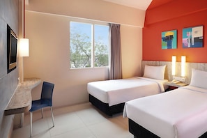 Habitación de hotel con dos camas, un escritorio, una silla, un televisor y obras de arte en la pared.
