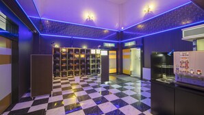 Een hotellobby met een zwart-wit schakeerdvloer, een automaat en een receptiegedeelte met een glazen scheidingswand.