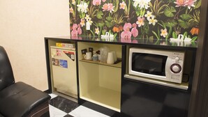 Een compacte kitchenette met een magnetron, een kleine koelkast en een plank met keukengerei.