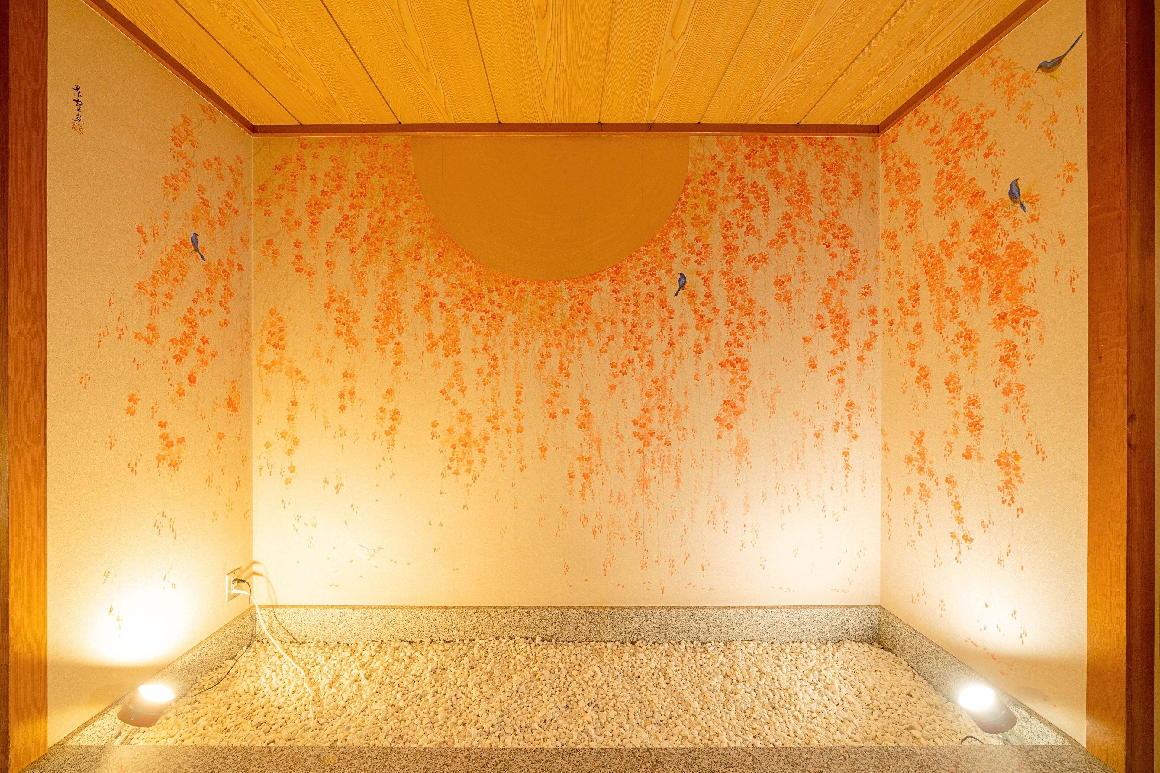 Quarto com teto de madeira, chão de pedrinhas e paredes com estampas florais em tons de laranja.