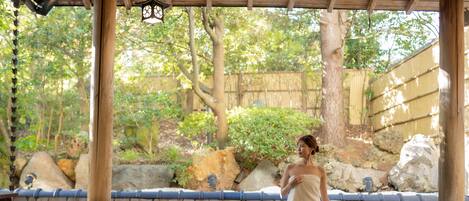 A person in a white towel standing in a stone pool with a wooden deck and bamboo fence in the background.