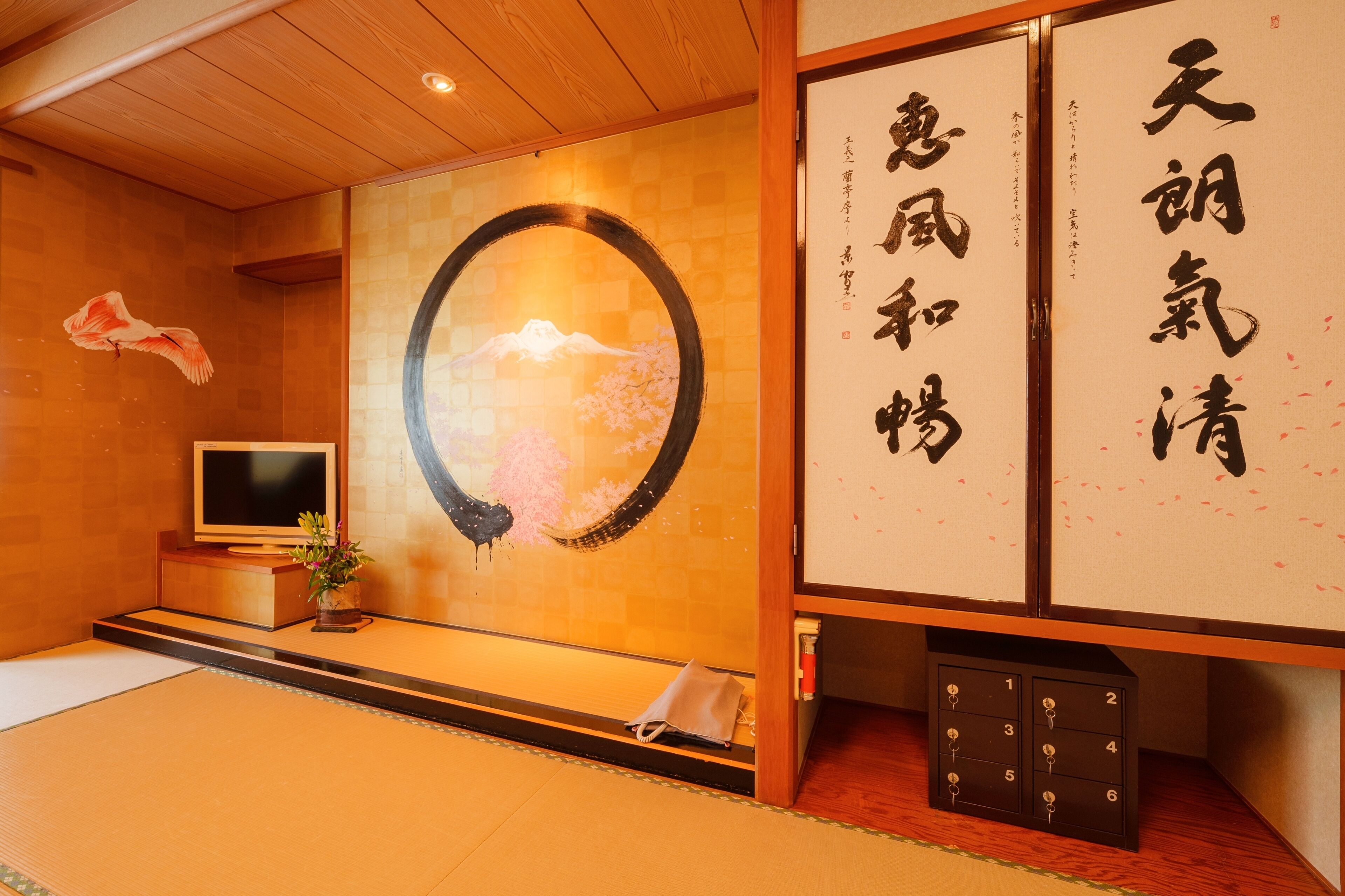 A traditional Japanese room with tatami flooring, a television, a decorative wall with calligraphy, and a wooden cabinet.