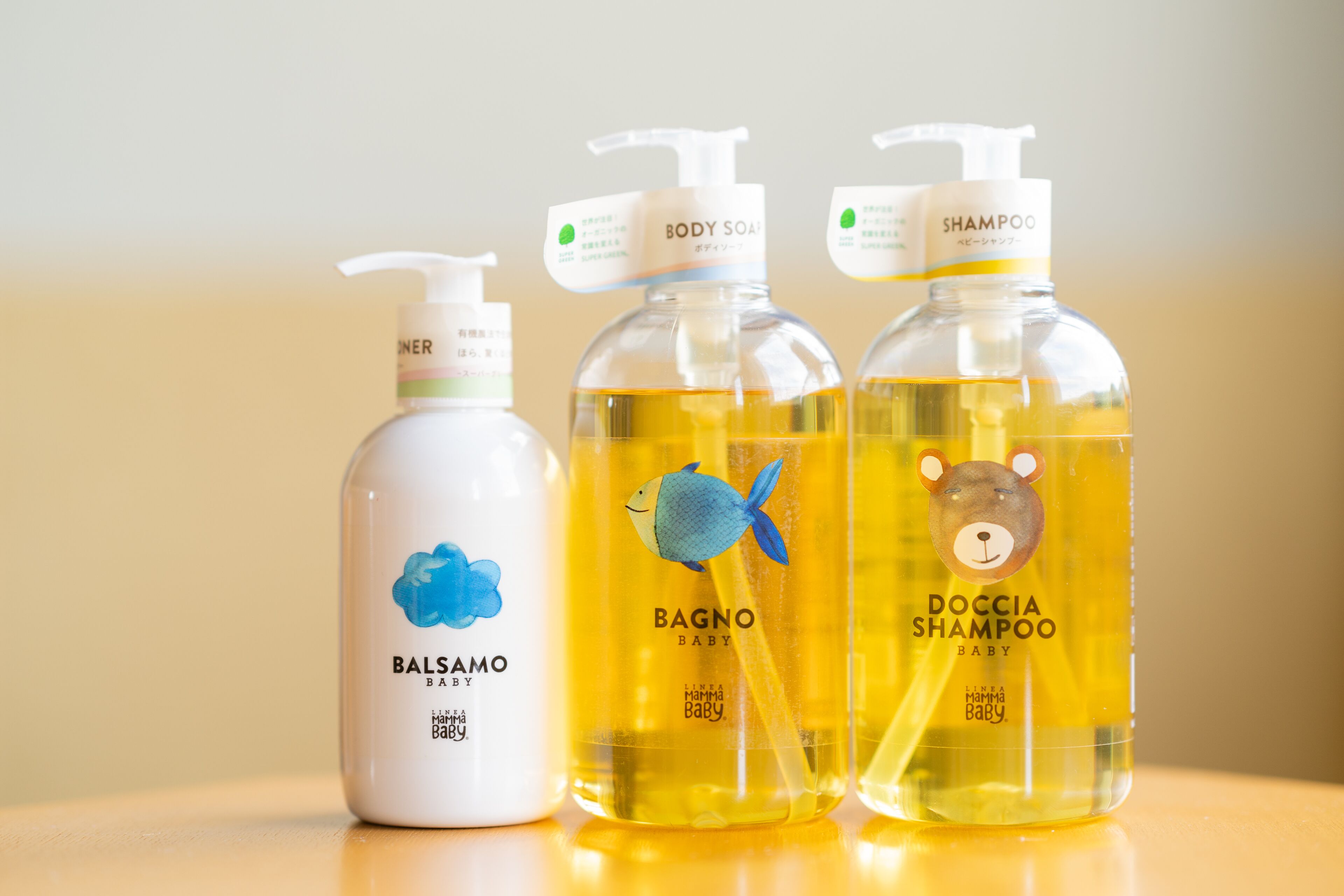 Three baby shampoo bottles with pump dispensers on a reflective surface.