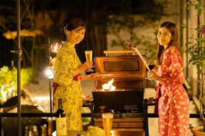 Two people grilling outdoors at night, holding drinks. - Hotel Hoho "A hotel overlooking the Echigo Plain and the Yahiko mountain range" (Niigata)