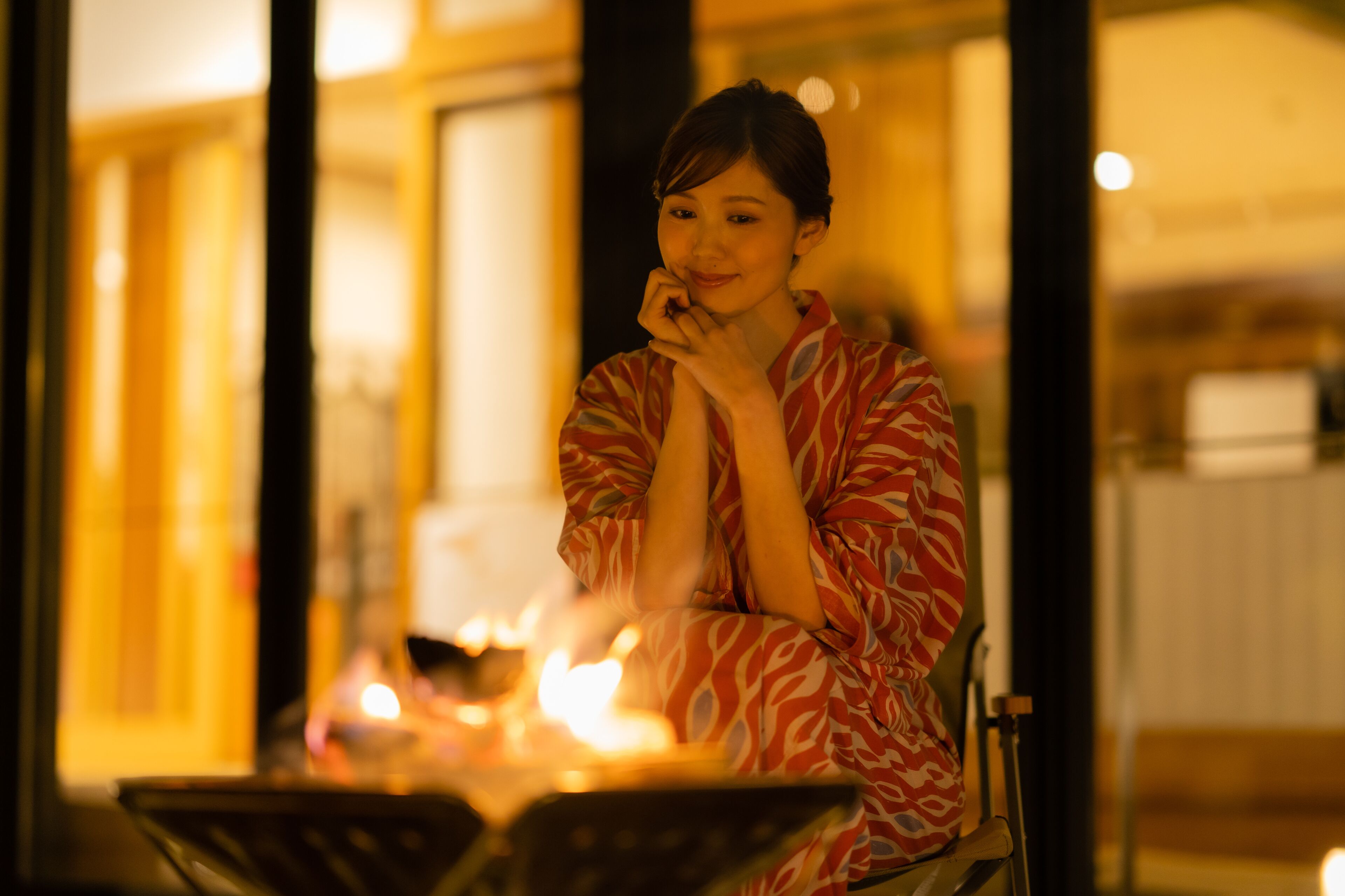A person sitting by a table with a lit candle, in a room with large windows and a warm interior.