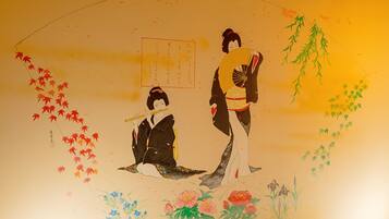 Una pintura japonesa tradicional con dos figuras, una sentada y otra de pie, rodeadas por elementos naturales como hojas y flores.