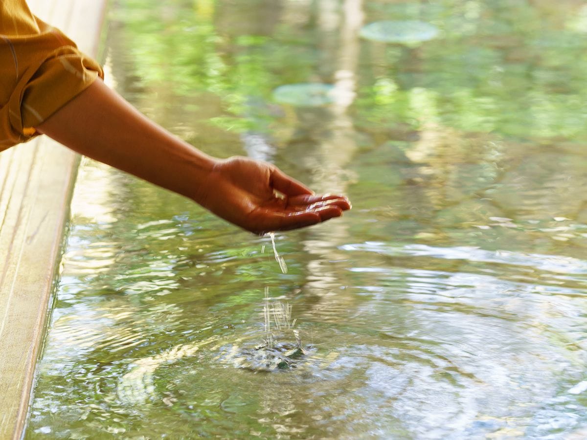 Eine Hand gießt Wasser aus einem Glas in eine klare Glaskugel.